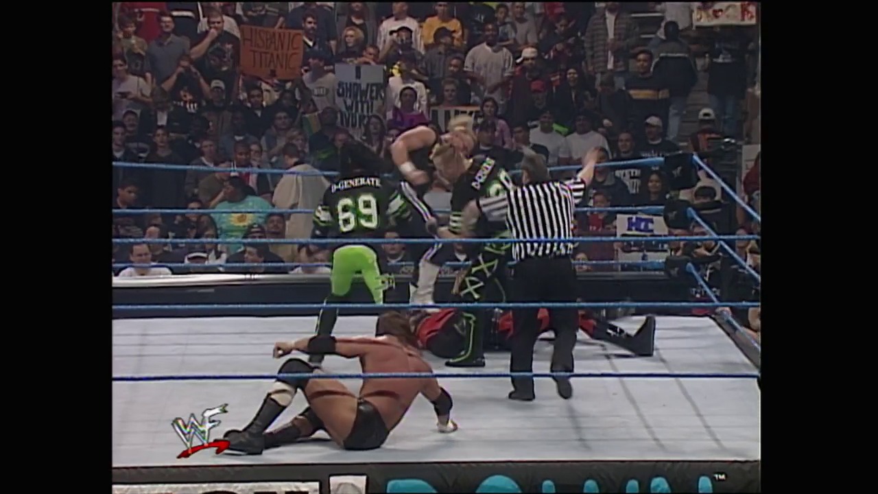 A frame from WWE SmackDown (February 17, 2000) at 26:42. A wrestler in black and lime green attire with number 69 grapples with an opponent near the ropes while a referee in striped shirt oversees the match. The crowd fills the arena stands in the background, with the WWF logo visible in the corner of the frame.