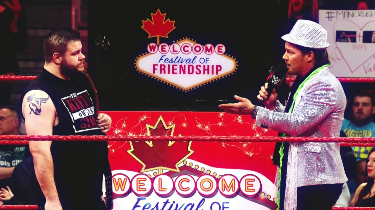 A frame from WrestleMania 33 (2017) at 44:02. Two wrestlers stand in a WWE ring during a segment themed "Welcome Festival of Friendship," with one holding a microphone wearing a sparkly jacket and fedora, while the other stands shirtless across from him. The backdrop features festive Las Vegas-style signage with Canadian maple leaf imagery.