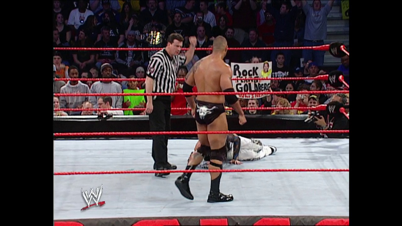 A frame from WWE Raw (April 7, 2003) at 40:51. A WWE Raw match in progress features a shirtless wrestler in black trunks standing in the red-roped ring while another wrestler lies on the mat. A referee in a striped shirt oversees the action as the crowd watches from the stands, with a "Rock vs Goldberg" sign visible in the background.