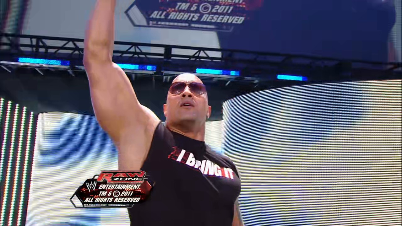 A frame from WWE Raw (February 14, 2011) at 1:41:27. A bald wrestler wearing sunglasses and a black "I Bring It" t-shirt raises his fist in the ring during WWE Raw. LED screens and the WWE Entertainment logo are visible in the background, dated 2011.