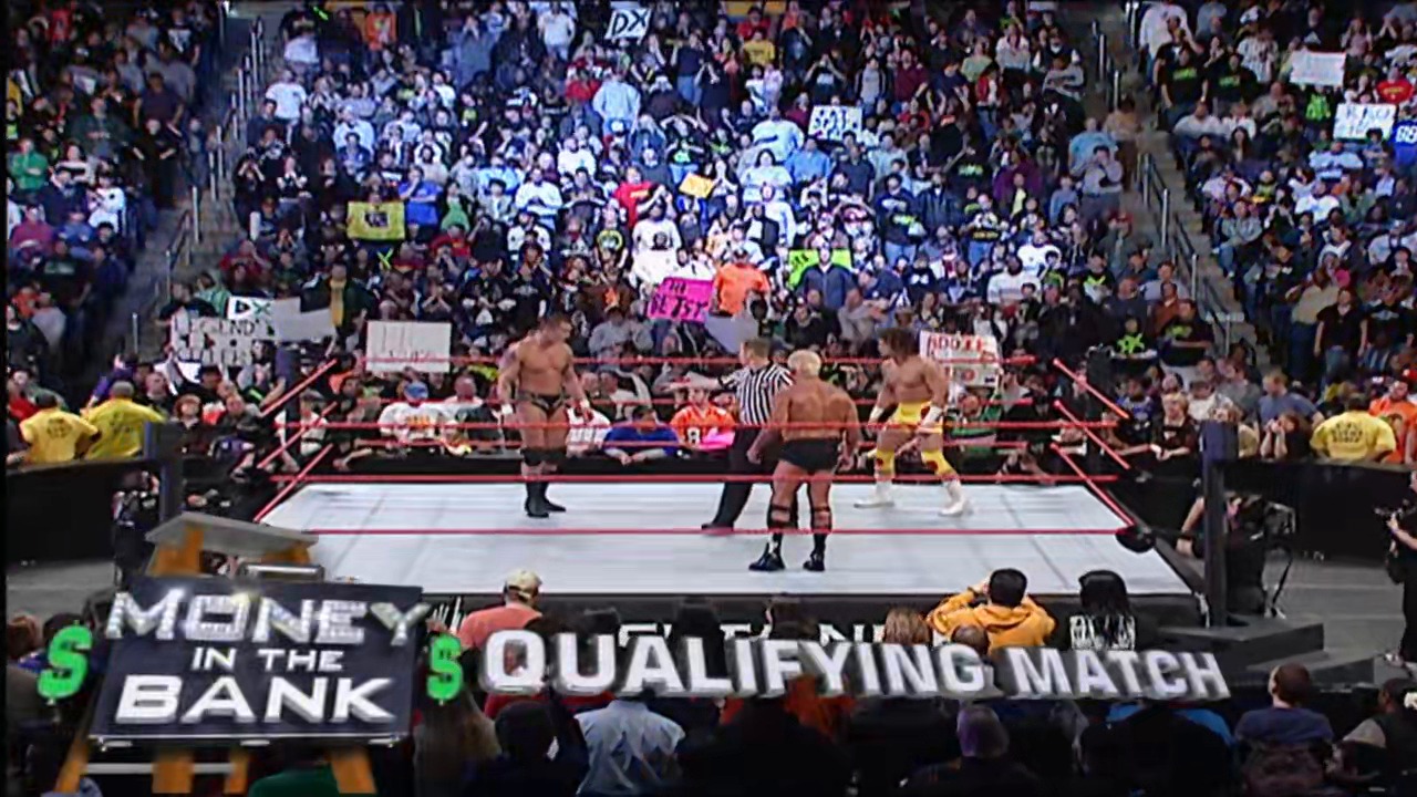 A frame from WWE Raw (March 12, 2007) at 14:14. A WWE wrestling match is underway in a packed arena, with multiple shirtless wrestlers competing in the ring while a referee officiates. Banners reading "Money in the Bank" and "Qualifying Match" are visible ringside, and the enthusiastic crowd fills the stands with signs and cheers.