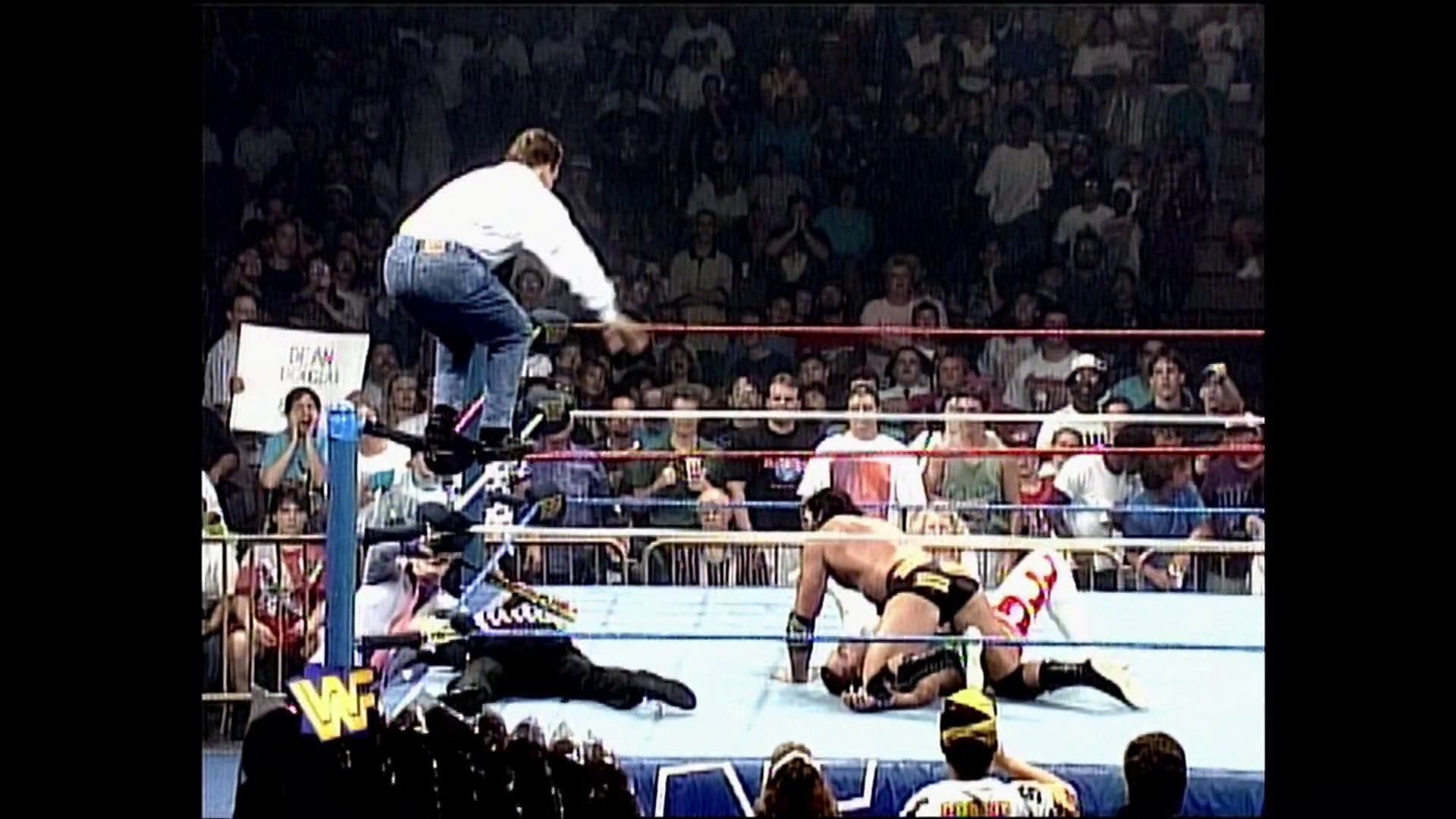 A frame from WWE Raw (September 21, 1995) at 0:25. A WWF wrestler in denim and a white shirt stands on the ring ropes while another wrestler lies on the mat below. The crowd fills the arena in the background, with the distinctive WWF logo visible in the corner of the frame.