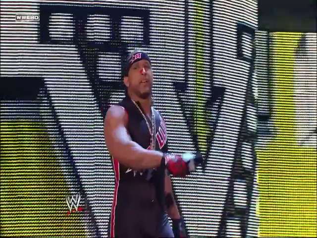 A frame from WWE SmackDown (August 13, 2010) at 59:33. A WWE wrestler stands in the ring wearing a red and black outfit with a bandana, positioned in front of an illuminated LED entrance screen displaying dynamic graphics with yellow and white lighting effects.