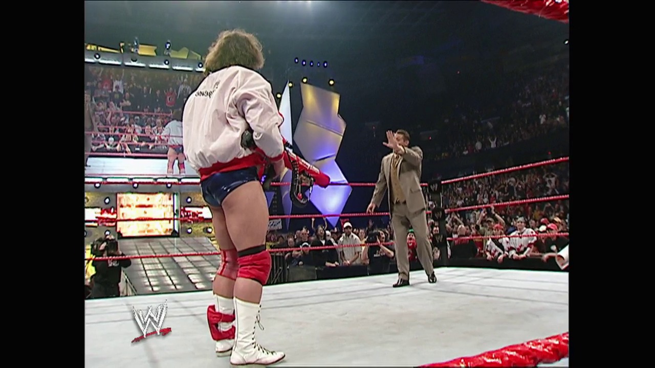 A frame from WWE Raw (April 19, 2004) at 1:06:09. A WWE wrestler in white and red attire stands in the ring facing a man in a tan suit, with a large crowd visible in the arena background and the WWE logo displayed in the lower left corner.