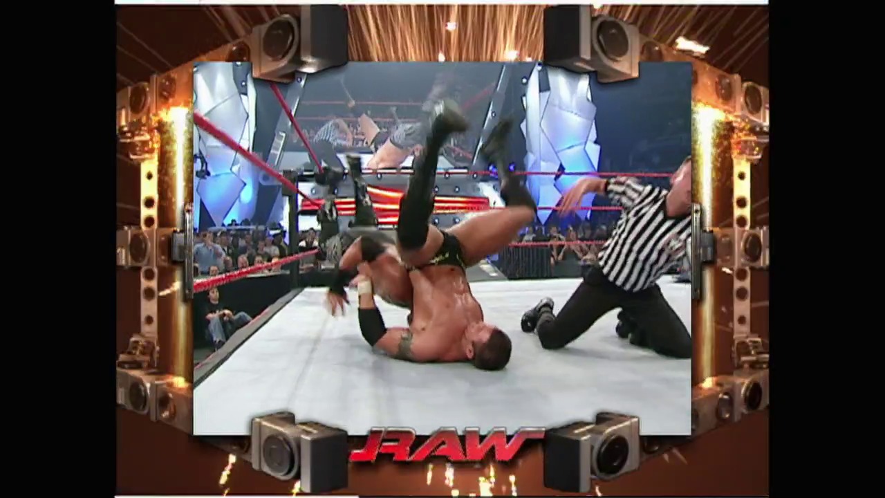A frame from WWE Raw (July 19, 2004) at 1:33:11. A wrestler performs an inverted move on the canvas during WWE Raw, with a referee in striped shirt officiating nearby. The arena features illuminated speaker columns, red ropes, an engaged crowd, and broadcast graphics displayed on screens above the ring.