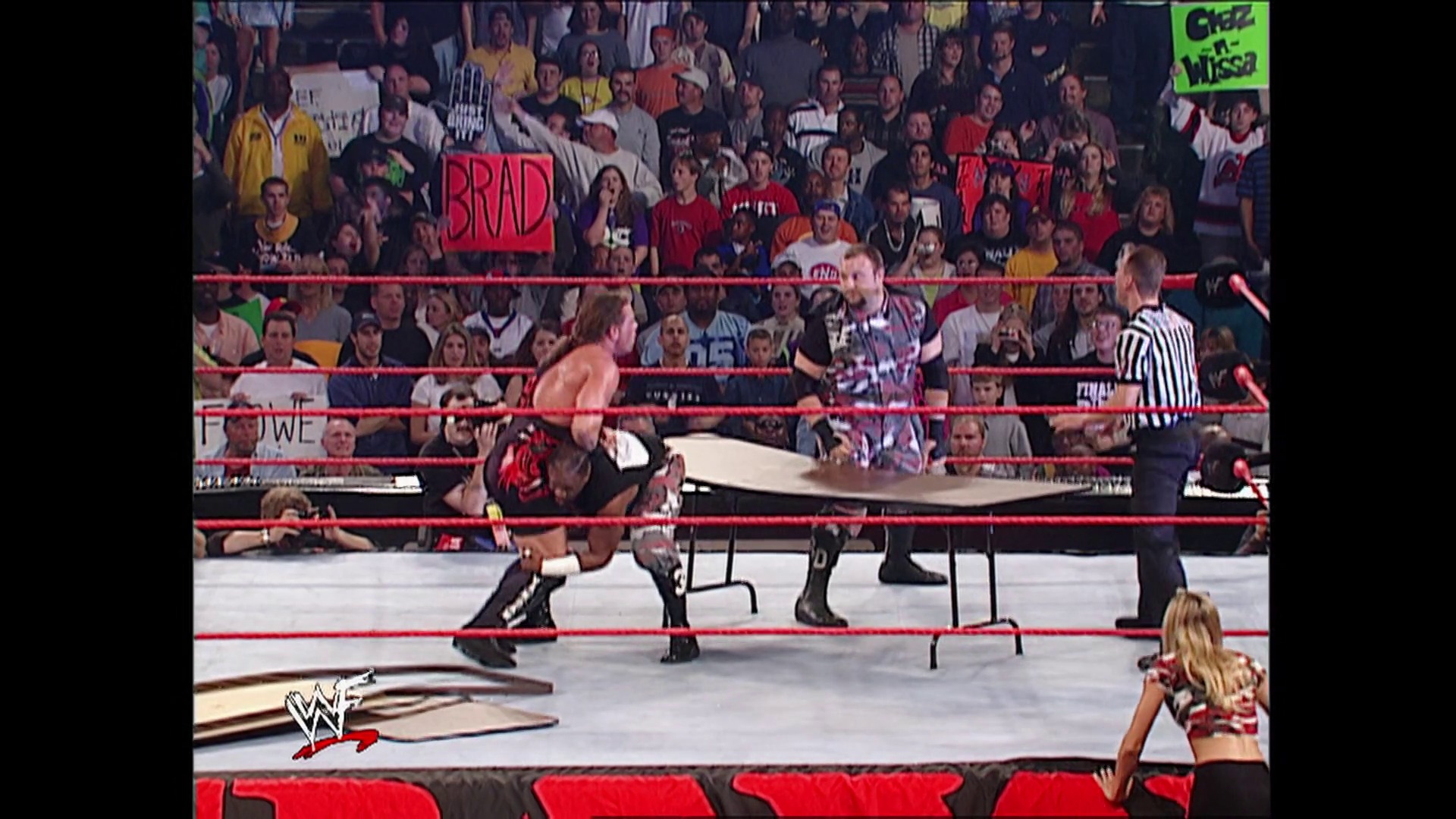 A frame from WWE Raw (November 19, 2001) at 30:02. A WWE Raw match in progress featuring wrestlers in the ring with a steel chair, a referee in striped shirt, and an engaged crowd in the background holding signs. The WWE logo is visible in the lower left corner of the broadcast.