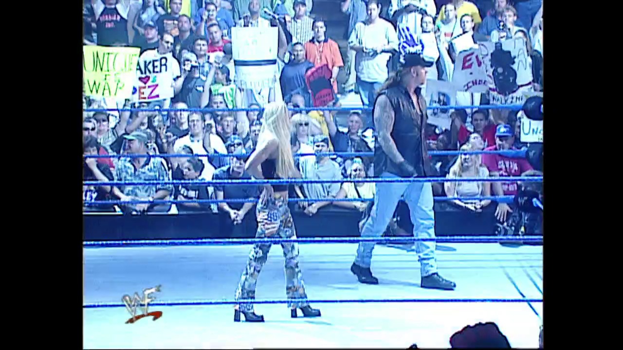 A frame from WWE SmackDown (June 21, 2001) at 1:05:18. A WWE wrestler in patterned attire stands in the ring facing an opponent, with the crowd visible in the bleachers behind them. The blue-roped wrestling ring and WWF logo are prominently displayed as fans hold signs along the barrier.