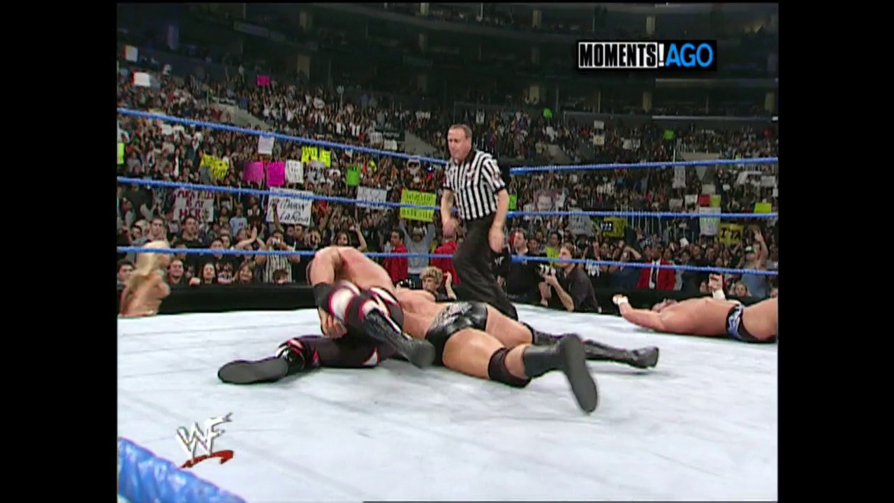 A frame from WWE SmackDown (October 12, 2000) at 52:47. A wrestler lies on the white mat in a WWE SmackDown ring while a referee in black and white stripes stands nearby. The crowd fills the arena in the background, with blue ropes framing the ring and the WWF logo visible at the bottom.