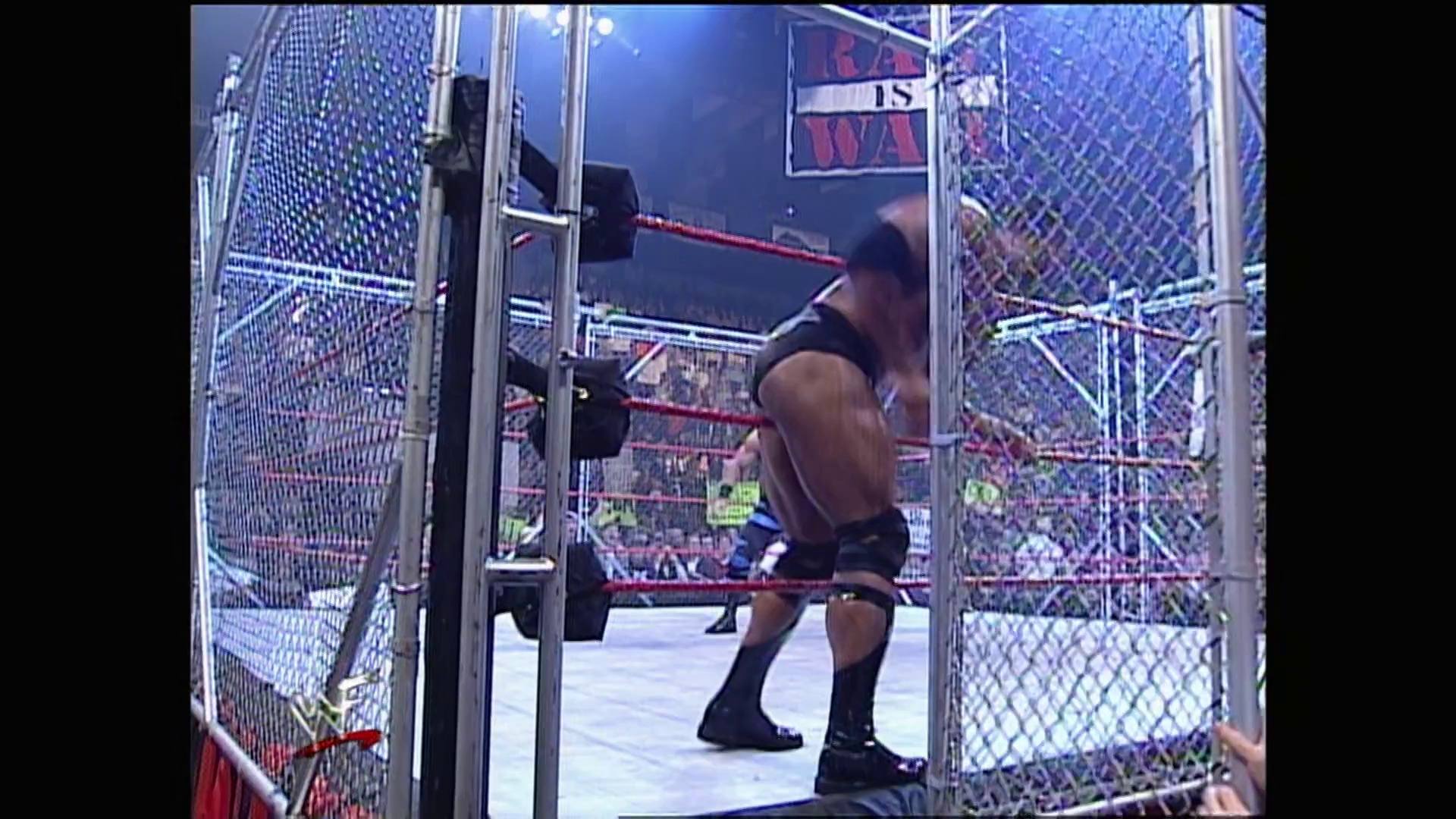 A frame from WWE Raw (March 6, 2000) at 1:22:07. A shirtless wrestler stands in a steel cage during a WWE Raw match, with the crowd and arena visible in the background. The cage structure and red ropes frame the wrestling ring, captured from inside the enclosed match setting.
