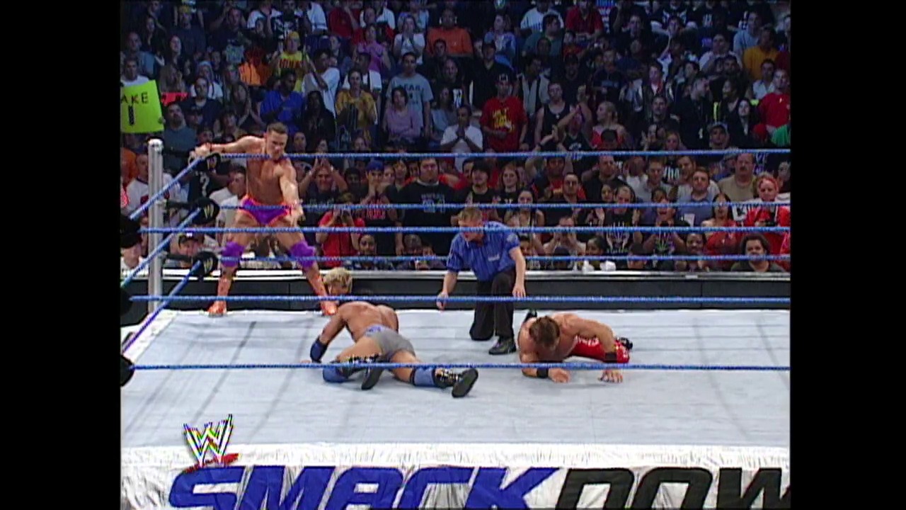 A frame from WWE Raw (October 10, 2002) at 35:52. A wrestler in purple and pink attire stands in the ring while two opponents lie on the mat below. The WWE SmackDown logo appears at the bottom, with a packed crowd visible in the background.