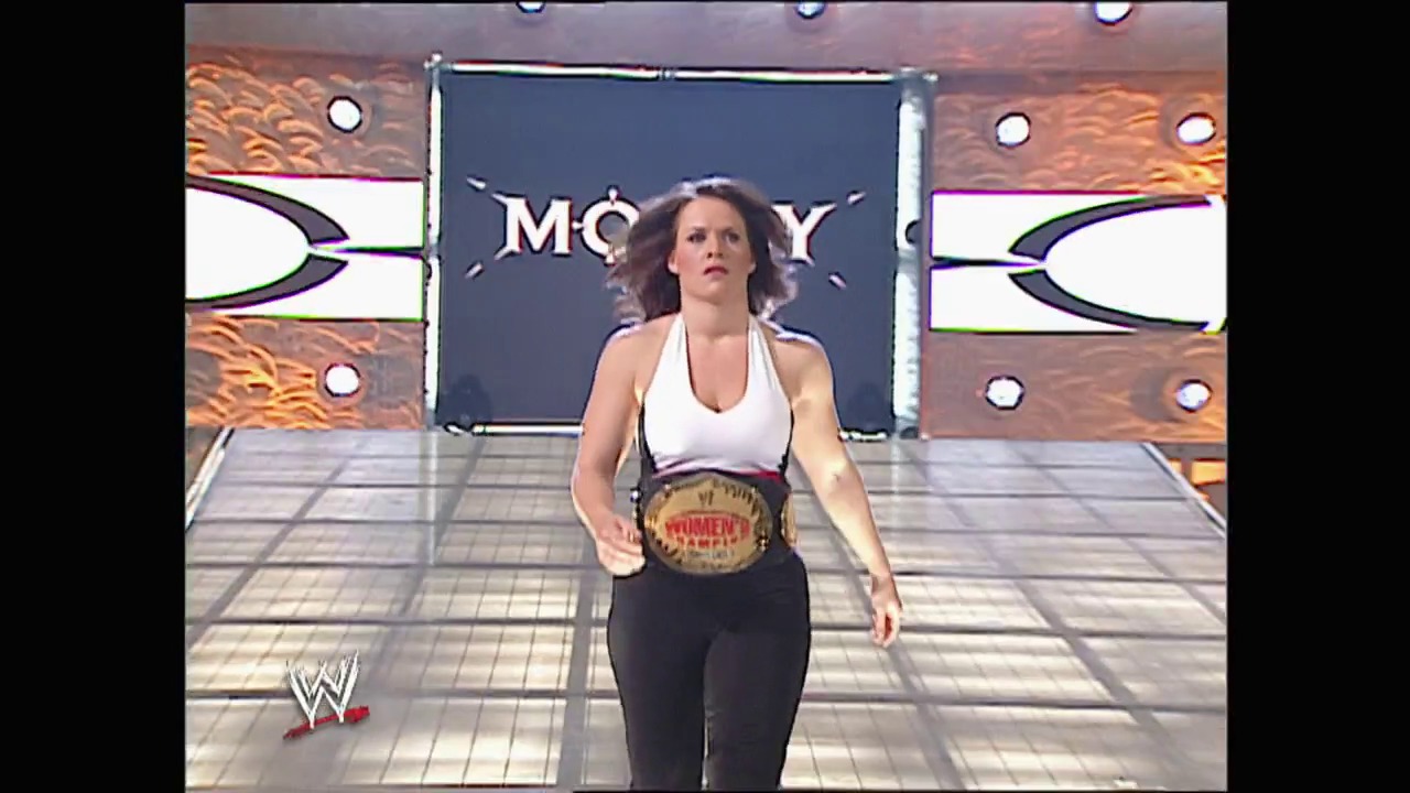 A frame from WWE Raw (September 1, 2003) at 39:18. A female wrestler stands in the WWE ring wearing a white halter top and black pants, displaying a championship belt around her waist. The arena features the distinctive "RAW" branding on the backdrop, with wood-textured paneling and metallic accents visible in the background.