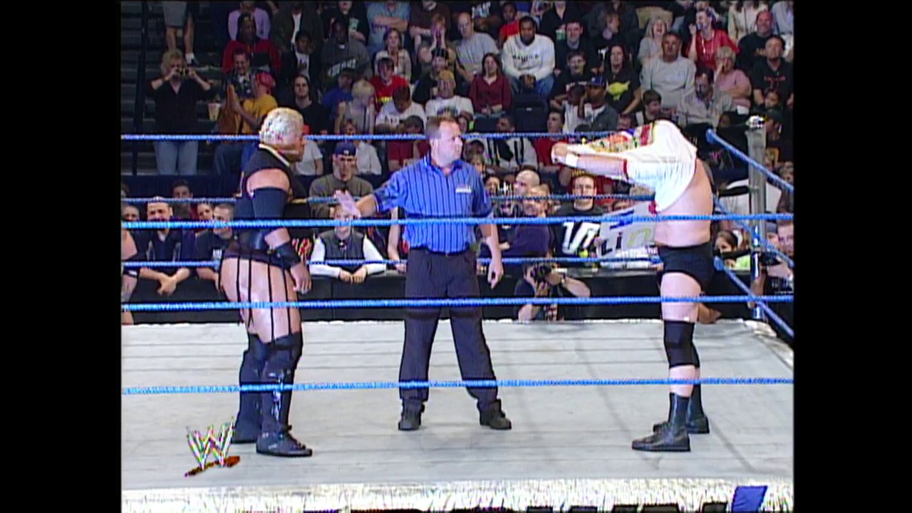 A frame from WWE SmackDown (April 24, 2003) at 36:43. Two wrestlers face off in a WWE SmackDown ring with a referee in a blue shirt officiating between them. The crowd fills the arena in the background while blue ropes frame the white canvas mat.