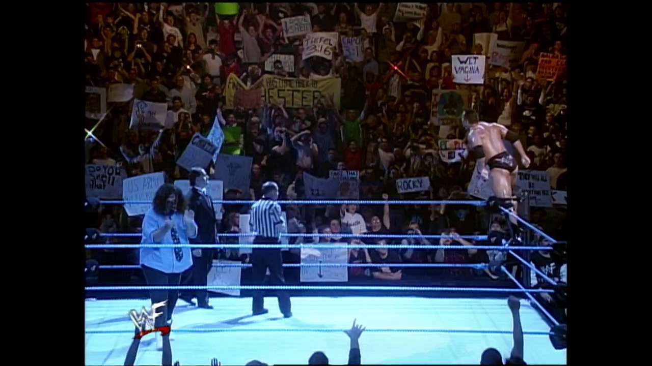 A frame from WWE SmackDown (November 25, 1999) at 41:47. A WWE wrestling match is in progress with two competitors in the ring, a referee in striped shirt, and an enthusiastic crowd holding signs in the background. The distinctive blue-lit WWE ring and arena setup are visible, capturing the energy of a late-1990s SmackDown event.