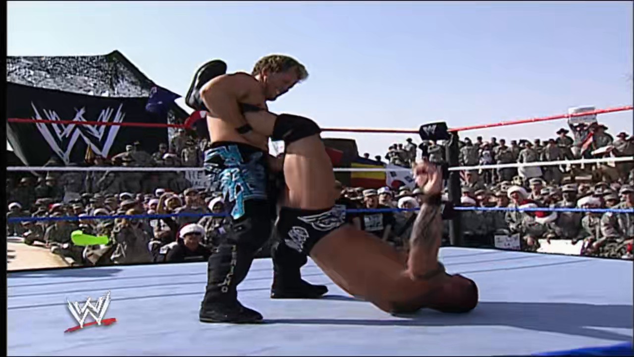 A frame from WWE Raw (December 24, 2007) at 14:15. A WWE wrestler executes a move on his opponent in the ring during a live event, with a large crowd visible in the background and the WWE logo displayed on the mat.