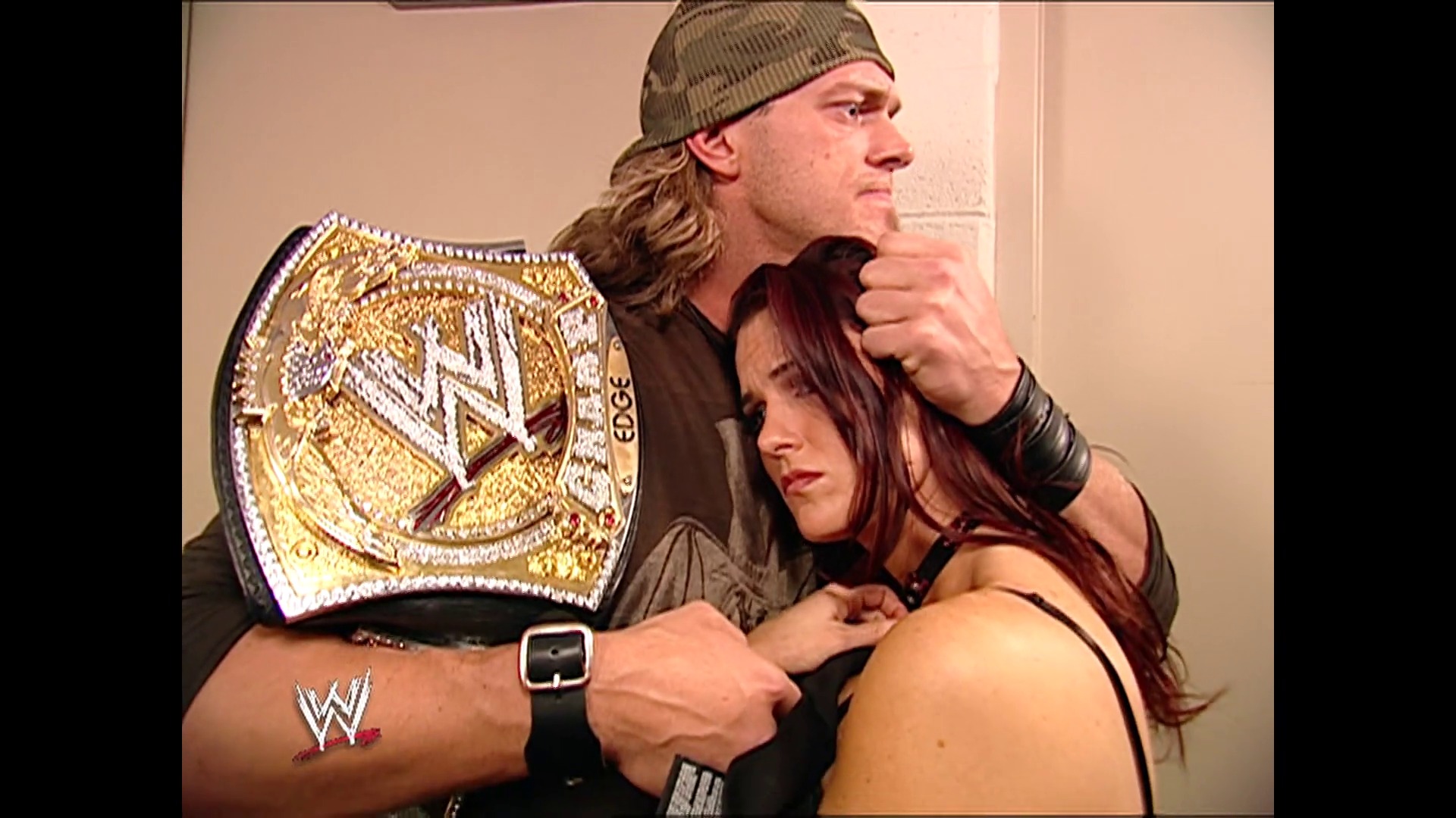 A frame from WWE Raw (January 23, 2006) at 28:34. A male wrestler wearing a beanie and brown shirt holds a championship belt while standing next to a female wrestler with dark reddish hair. The WWE logo is visible on the wrestler's arm, indicating this is from a professional wrestling broadcast.