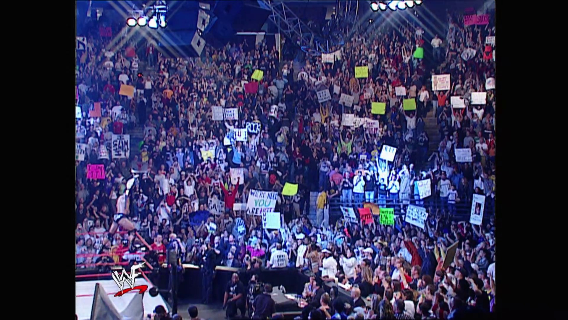 A frame from WWE Raw (November 19, 2001) at 46:52. # WWE Raw Arena Scene

A packed indoor arena filled with thousands of enthusiastic fans holding colorful signs and wearing bright clothing. The WWE logo is visible in the lower left corner, with stage lighting illuminating the crowd during this televised wrestling event.