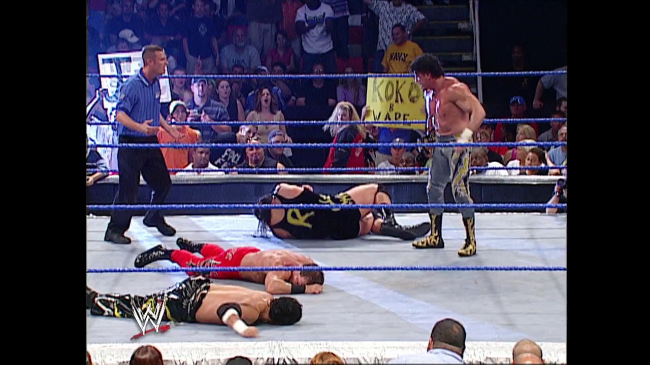 A frame from WWE SmackDown (August 21, 2003) at 1:11:34. A WWE wrestling match in progress with multiple wrestlers down on the mat, a referee overseeing the action, and a packed crowd visible behind the blue ropes. The WWE logo is visible in the corner of the ring.