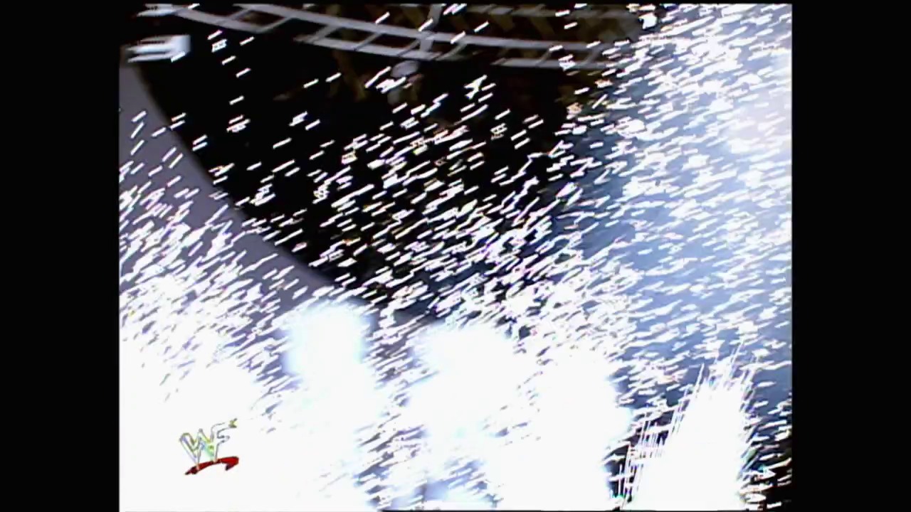 A frame from WWE SmackDown (November 11, 1999) at 0:45. A WWE wrestling ring is captured mid-action with motion blur effects, showing the squared circle from an elevated angle. The WWF logo is visible in the lower left corner, with the crowd and arena structure visible in the background.