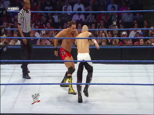 A frame from WWE SmackDown (September 24, 2010) at 35:11. Two shirtless wrestlers engage in combat inside a WWE ring, with one wearing red and gold trunks and the other in black pants. A referee in striped shirt supervises while the crowd watches from the stands, with WWE branding visible on the canvas and broadcast graphics.