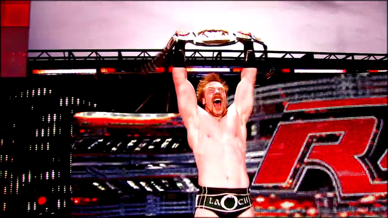 A frame from Royal Rumble (2010) at 0:27. # Royal Rumble 2010 Frame

A shirtless wrestler triumphantly holds a championship belt overhead in the ring, with an intense expression on his face. The arena is illuminated with red and blue lighting, digital displays, and a large video screen in the background showing the event graphics.