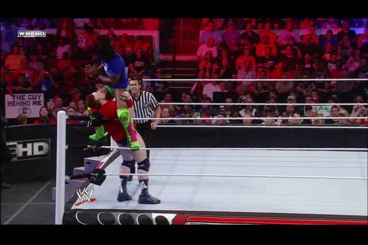 A frame from WWE Raw (April 25, 2011) at 39:45. A wrestler in neon green and black attire executes a move in the WWE ring while a referee officiates. The packed arena glows in red lighting, with spectators visible throughout the crowd and signage along the ringside.