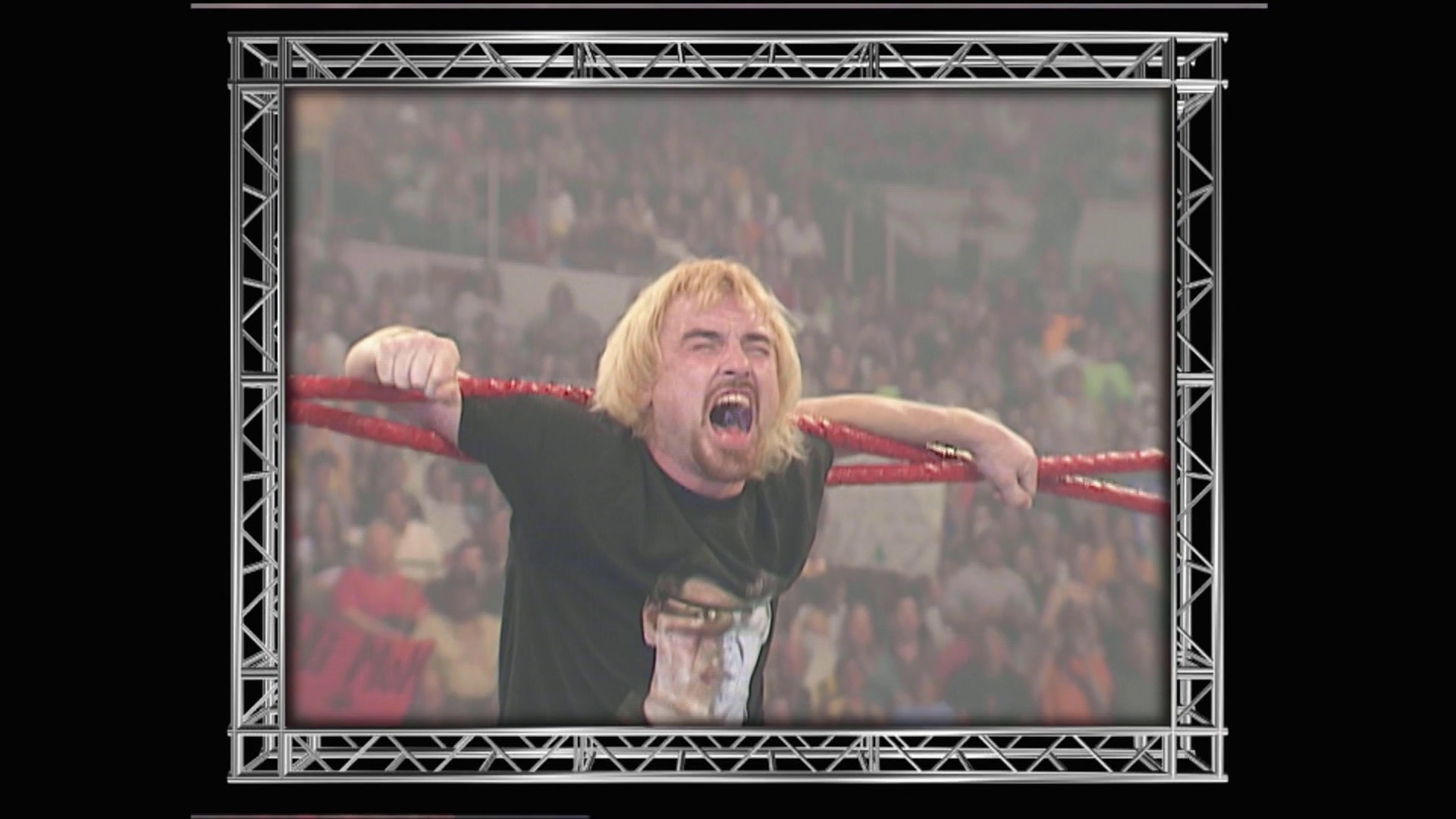 A frame from WWE Raw (July 16, 2001) at 14:34. A blonde-haired wrestler in a black shirt and white pants stands in a WWE ring with red ropes, arms outstretched in an aggressive pose while a large crowd fills the blurred arena background behind him.