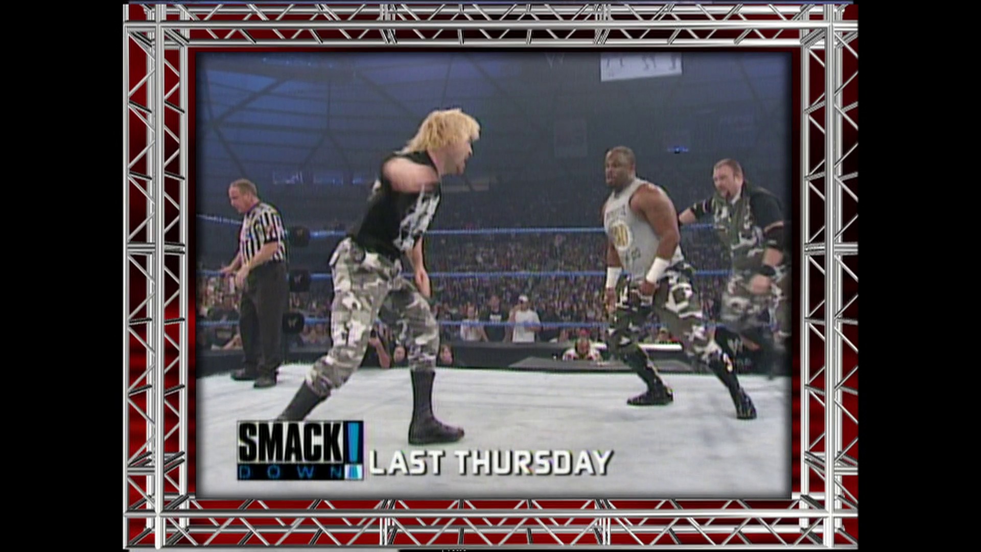 A frame from WWE Raw (July 9, 2001) at 13:14. A WWE wrestling match is underway in the ring with multiple wrestlers in combat gear facing off, while a referee oversees the action. The "SmackDown" logo and "Last Thursday" text appear at the bottom of the screen, with the crowd visible in the background under arena lighting.