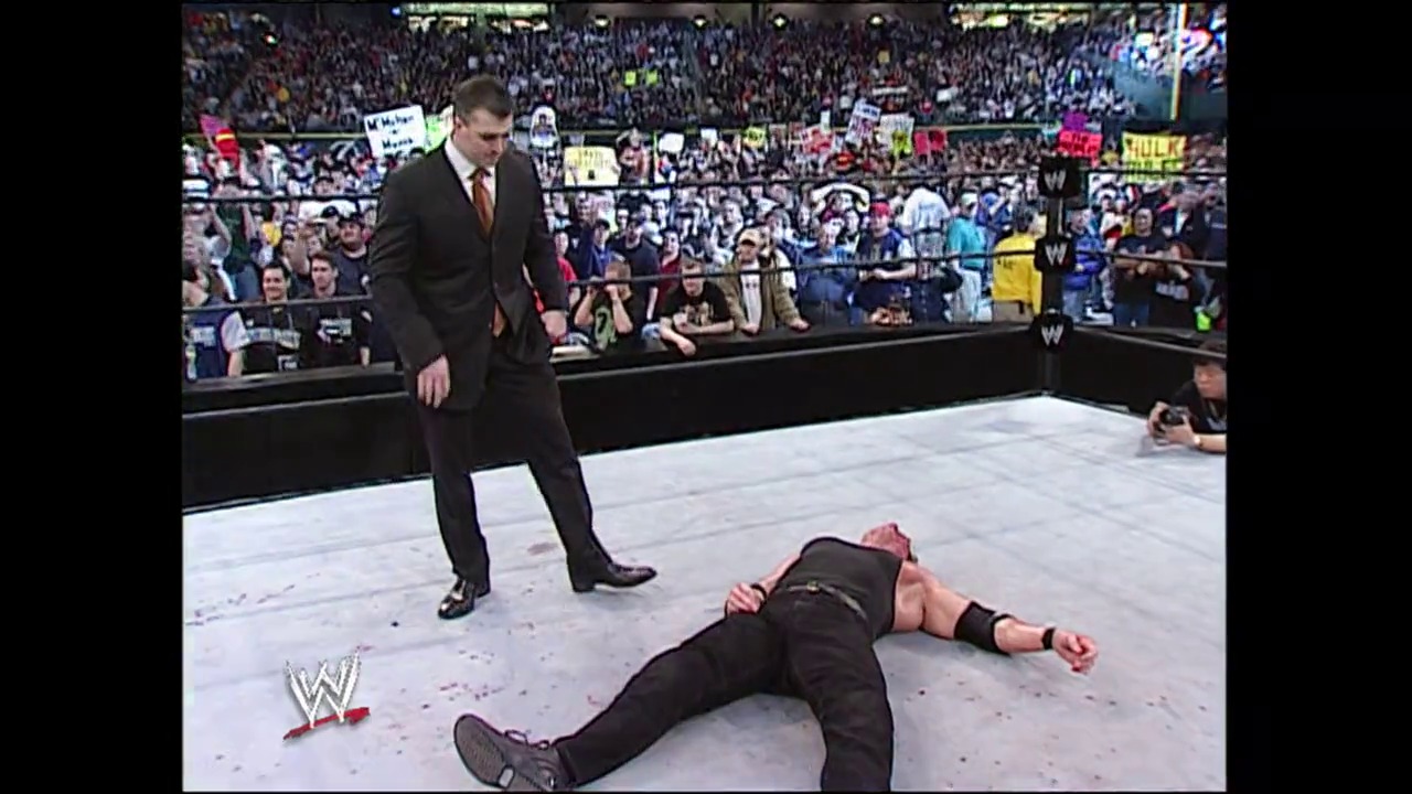 A frame from WrestleMania XIX (2003) at 2:41:18. # WrestleMania XIX Frame

A suited official stands over a fallen wrestler lying on the mat in a WWE ring. The packed stadium crowd fills the background, with the WWE logo visible in the corner.