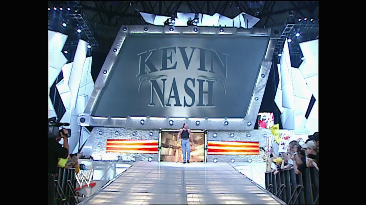 A frame from WWE Raw (April 14, 2003) at 0:59. A WWE Raw wrestling entrance stage features "KEVIN NASH" displayed prominently above, with red and gold lighting effects flanking the sides. The elevated ramp leads to the ring as crowd members line both sides of the stage.
