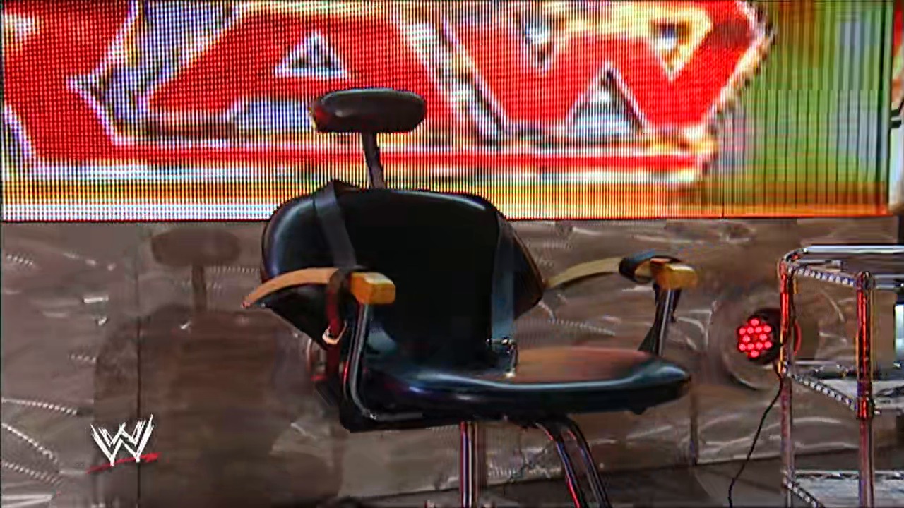 A frame from WWE Raw (February 26, 2007) at 39:26. A black office chair with orange accents sits prominently in the WWE Raw ring, with the distinctive WWE logo visible in the lower left corner and a colorful red graphic display visible in the background.
