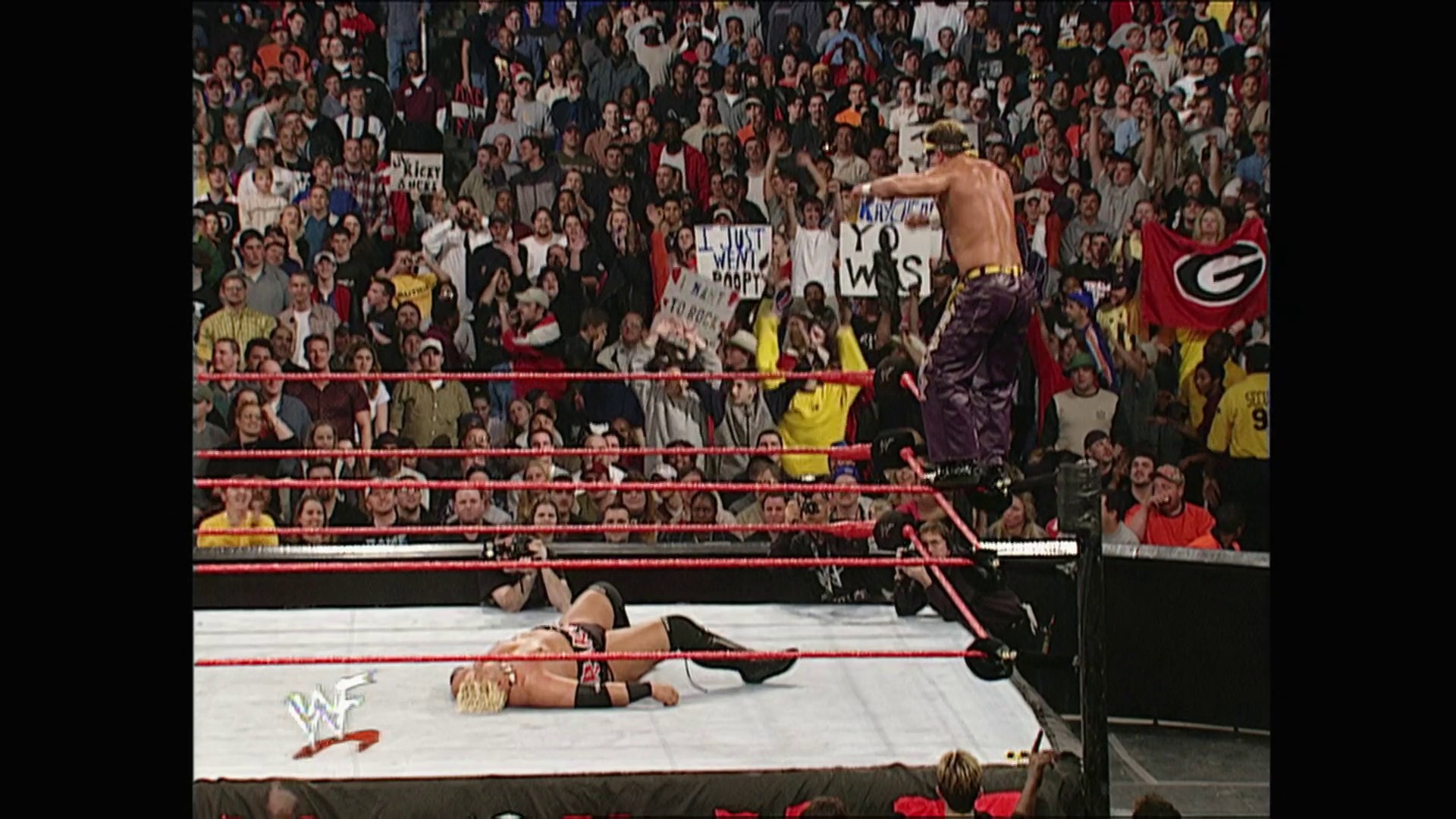 A frame from WWE Raw (February 5, 2001) at 1:07:54. A WWE wrestler stands shirtless on the ring apron while another lies on the mat below. The packed crowd holds signs and cheers behind the red ropes, with the WWF logo visible in the corner.