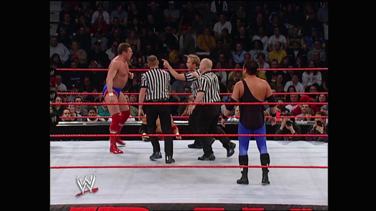 A frame from WWE Raw (January 13, 2003) at 25:51. Two wrestlers face off in a WWE Raw ring surrounded by red ropes, with two referees in striped shirts between them. A packed crowd watches from the stands while the WWE logo appears in the lower left corner.