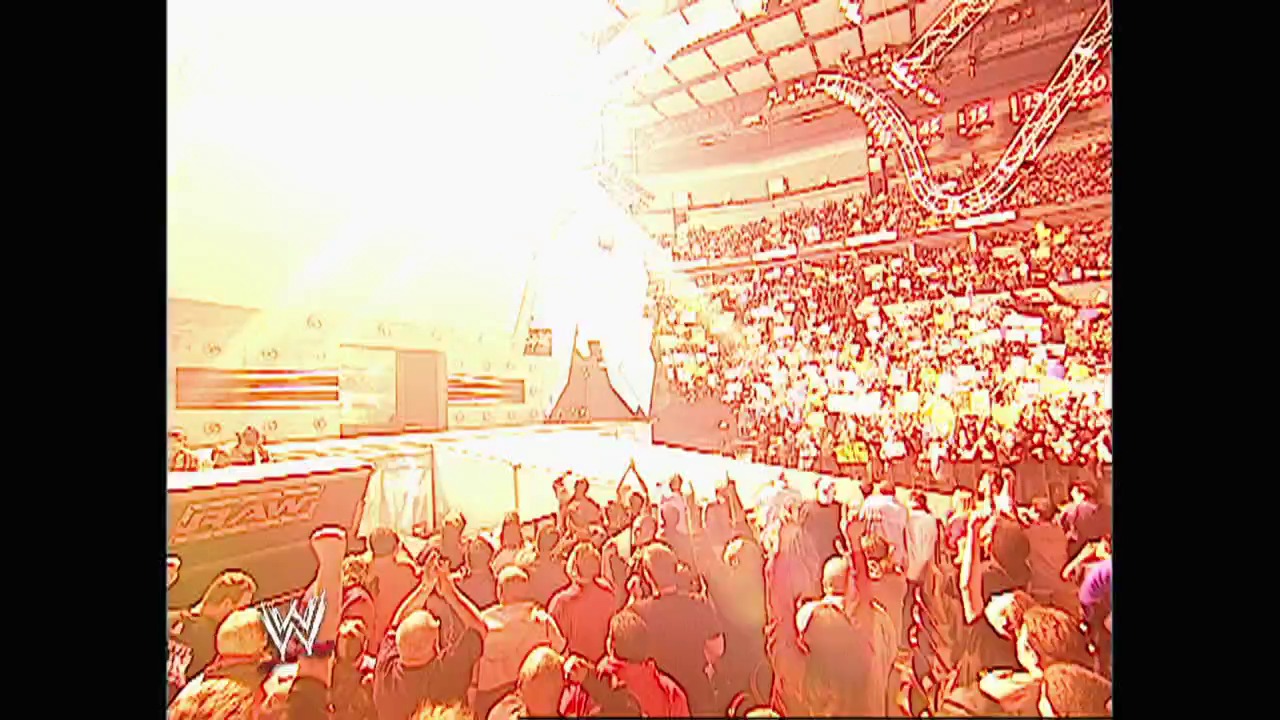 A frame from WWE Raw (February 9, 2004) at 0:48. A packed WWE arena during Raw, with thousands of enthusiastic fans filling the stands. The wrestling ring is visible in the center with performers, while the WWE logo is displayed on the arena signage, capturing the energy of a live televised wrestling event.