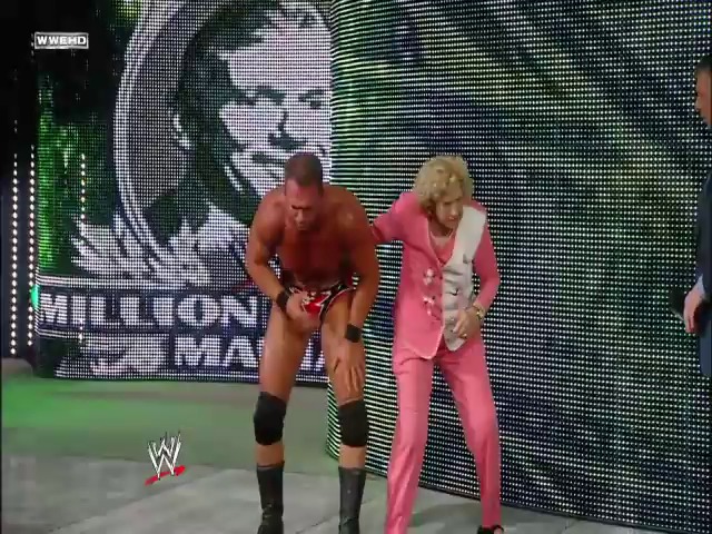 A frame from WWE Raw (June 9, 2008) at 26:34. A WWE wrestler in red attire stands on the entrance ramp next to a woman in a pink suit, with a large LED screen displaying a wrestler's face and "Million Dollar Man" text visible in the background.