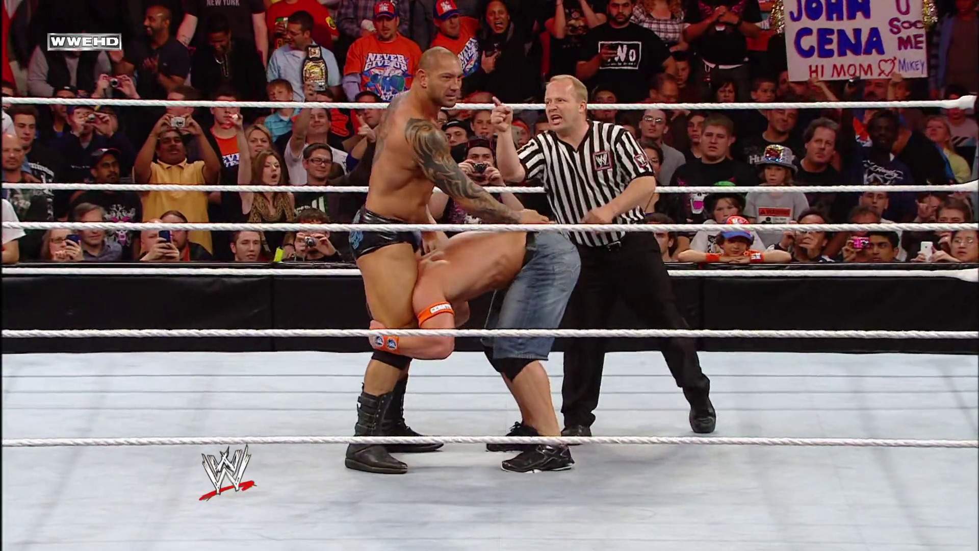 A frame from WWE Raw (May 17, 2010) at 1:59:44. # WWE Raw Match Scene

A shirtless wrestler performs a move on an opponent in jeans inside the WWE ring, while a referee in striped shirt officiates. The crowd fills the arena behind the ropes, with visible signs and the WWE logo displayed at the bottom of the screen.