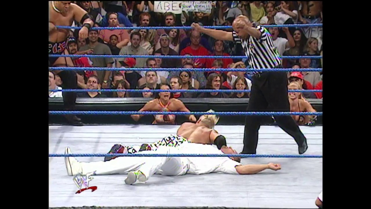 A frame from WWE SmackDown (September 14, 2000) at 40:30. A WWE wrestler lies on the mat while a referee in a striped shirt stands over him during a match. The blue-roped ring is surrounded by an enthusiastic crowd, with other wrestlers visible in the background along the ring apron.