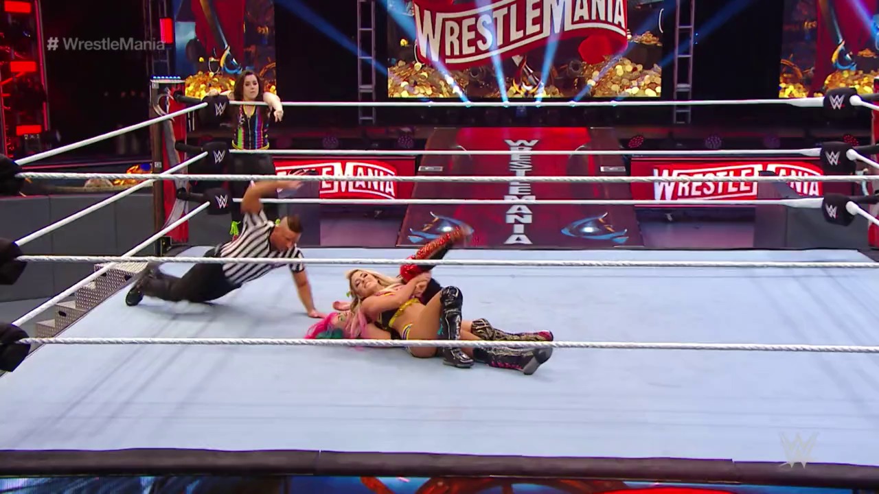 A frame from WrestleMania 36 (2020) at 17:35. A wrestler lies pinned on the WrestleMania ring mat while a referee makes the count, with another wrestler standing at the ringside and promotional graphics visible on the surrounding barriers and screens above.