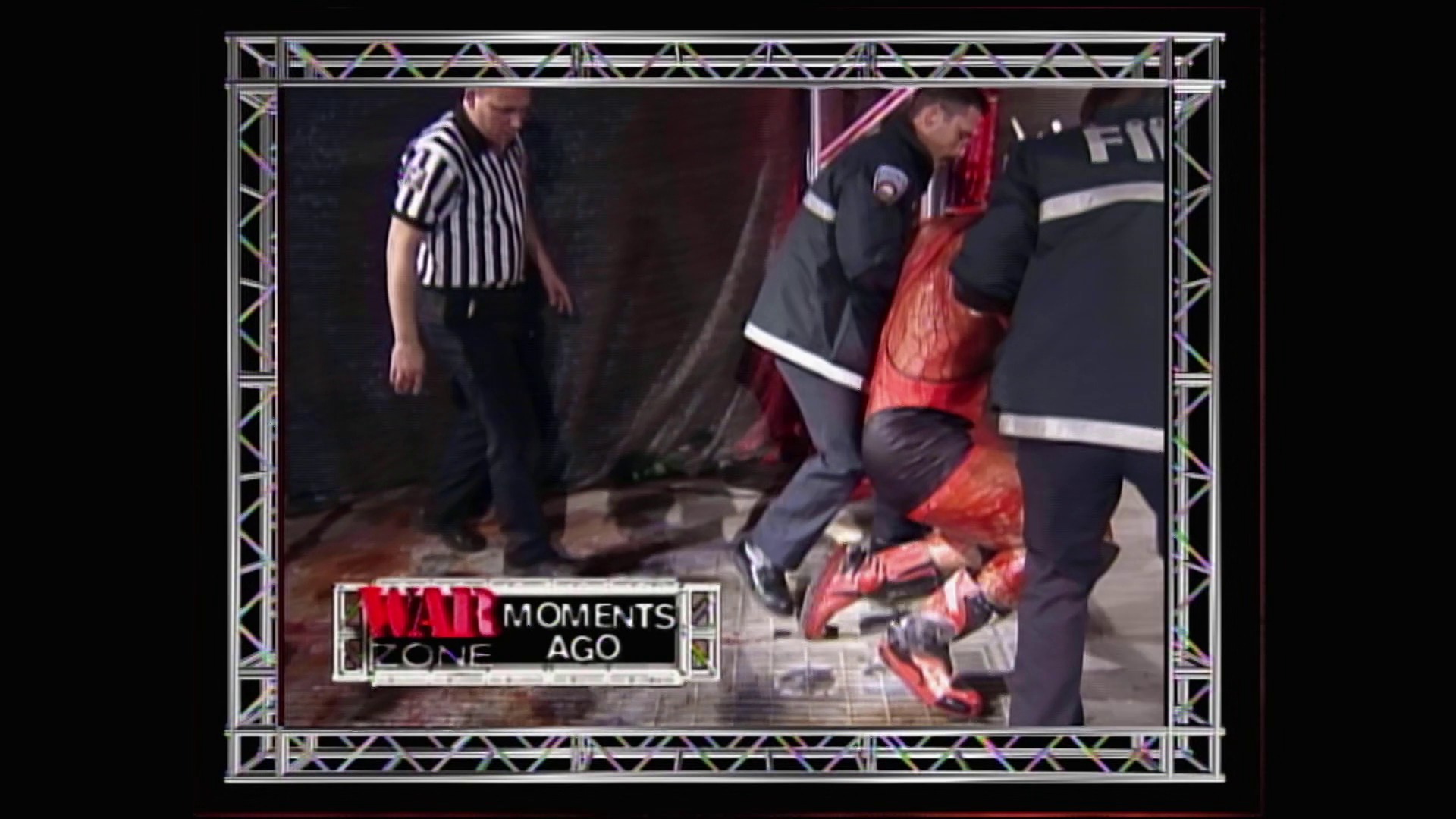 A frame from WWE Raw (December 14, 1998) at 1:09:32. A wrestler in a red outfit is being attended to on the mat by officials and a referee in a striped shirt during a WWE Raw match. The "War Zone Moments Ago" graphic appears at the bottom of the screen.