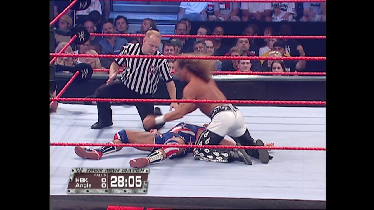 A frame from WWE Raw (October 3, 2005) at 21:23. A WWE wrestler in white and black attire lies on the mat while an opponent stands nearby, with a referee in a striped shirt overseeing the match. The scoreboard displays "28:05" timing information, and the red-roped ring is surrounded by spectators in the arena.