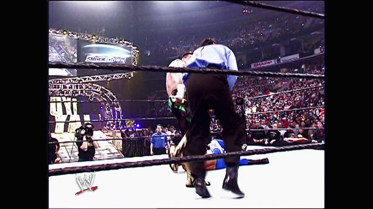 A frame from WWE No Way Out (2004) at 1:04:22. A wrestler in blue and white attire is draped over the top rope of the WWE ring during an intense match, with a large crowd visible in the background and the WWE logo displayed at the bottom of the frame.