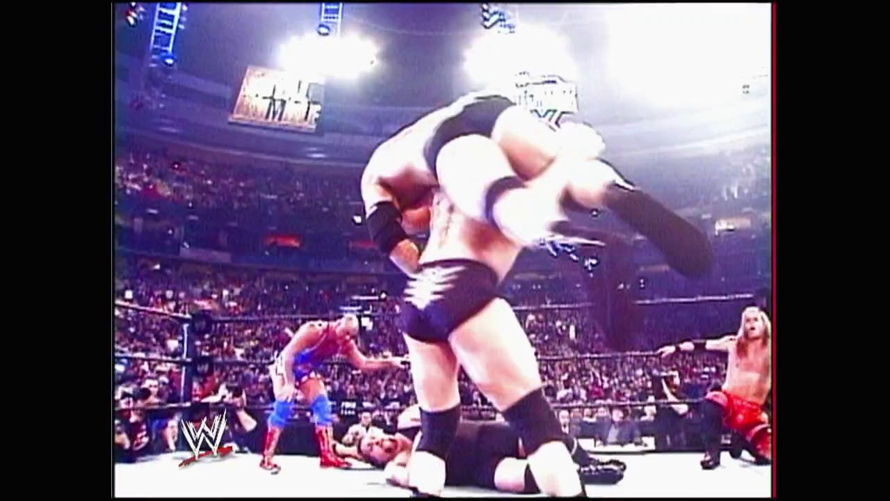 A frame from WWE Raw (March 8, 2004) at 52:38. A wrestler in white and black attire performs an aerial move in the WWE ring, while opponents lie on the mat below. The packed arena crowd watches under bright stadium lights, with the WWE logo visible on the ring apron.