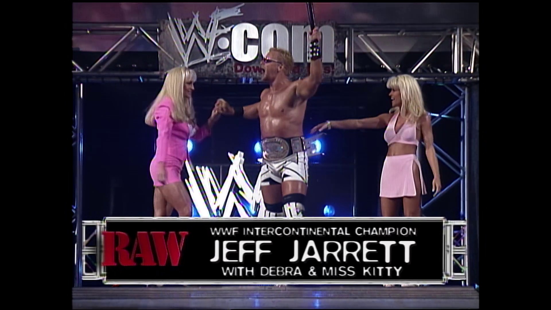 A frame from WWE Raw (September 13, 1999) at 14:48. # Visual Description

A shirtless male wrestler celebrates in the ring while holding the WWF Intercontinental Championship belt, flanked by two blonde women in pink attire. The WWE Raw logo and chyron identifying him as "Jeff Jarrett with Debra & Miss Kitty" are displayed on screen.