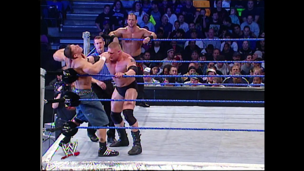 A frame from WWE SmackDown (November 13, 2003) at 1:11:35. A WWE wrestler executes a move against an opponent in the blue-roped ring while a third wrestler stands in the background. The crowd fills the arena stands, and WWE graphics are visible at the bottom of the screen.