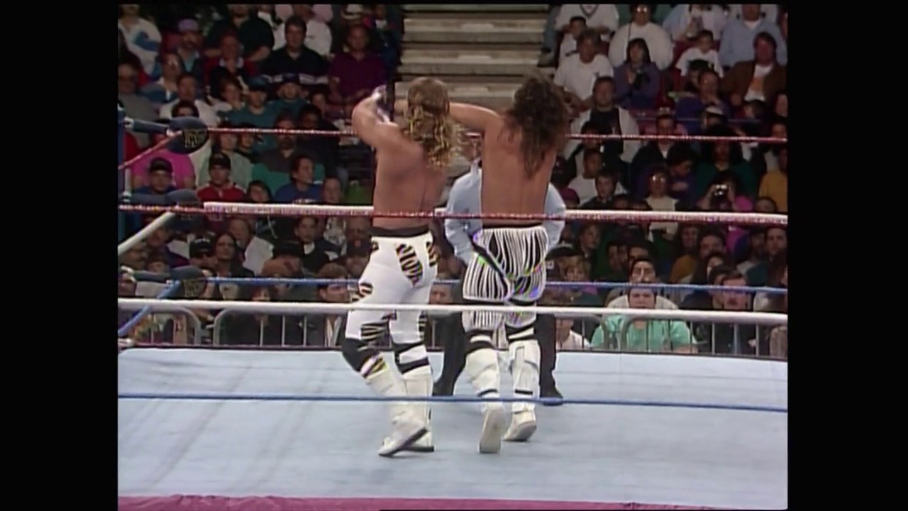 A frame from Royal Rumble (1993) at 26:33. Two shirtless wrestlers grapple in a WWE ring during the 1993 Royal Rumble, with a packed crowd visible in the background behind the ropes and protective barriers.