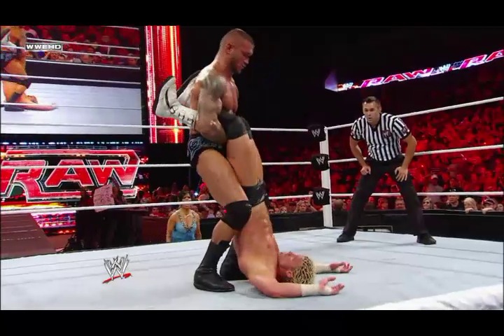 A frame from WWE Raw (August 29, 2011) at 25:39. A WWE wrestler delivers an attack to his opponent on the mat during Raw, while a referee monitors the action. The illuminated red ring, crowd in the background, and WWE graphics are visible in this professional wrestling broadcast.