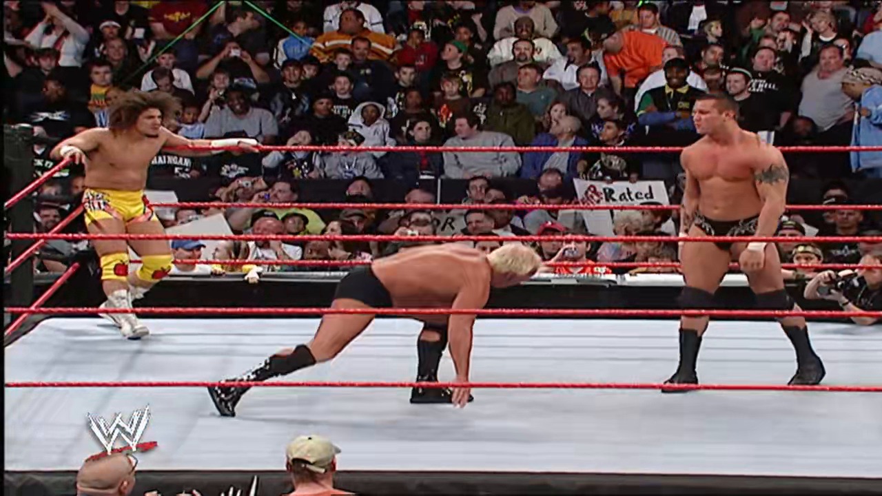 A frame from WWE Raw (March 12, 2007) at 14:46. A WWE Raw match in progress features three shirtless wrestlers in a red-roped ring with a packed crowd visible in the background. One wrestler is bent over in the center of the ring while two others stand nearby, ready for action.