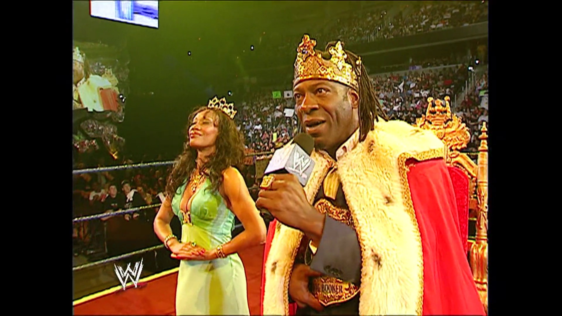 A frame from WWE SmackDown (August 18, 2006) at 1:20:03. A WWE wrestler in an elaborate gold and red royal outfit with a crown holds a microphone in the ring, accompanied by a woman in a green dress. The packed arena crowd is visible in the background.