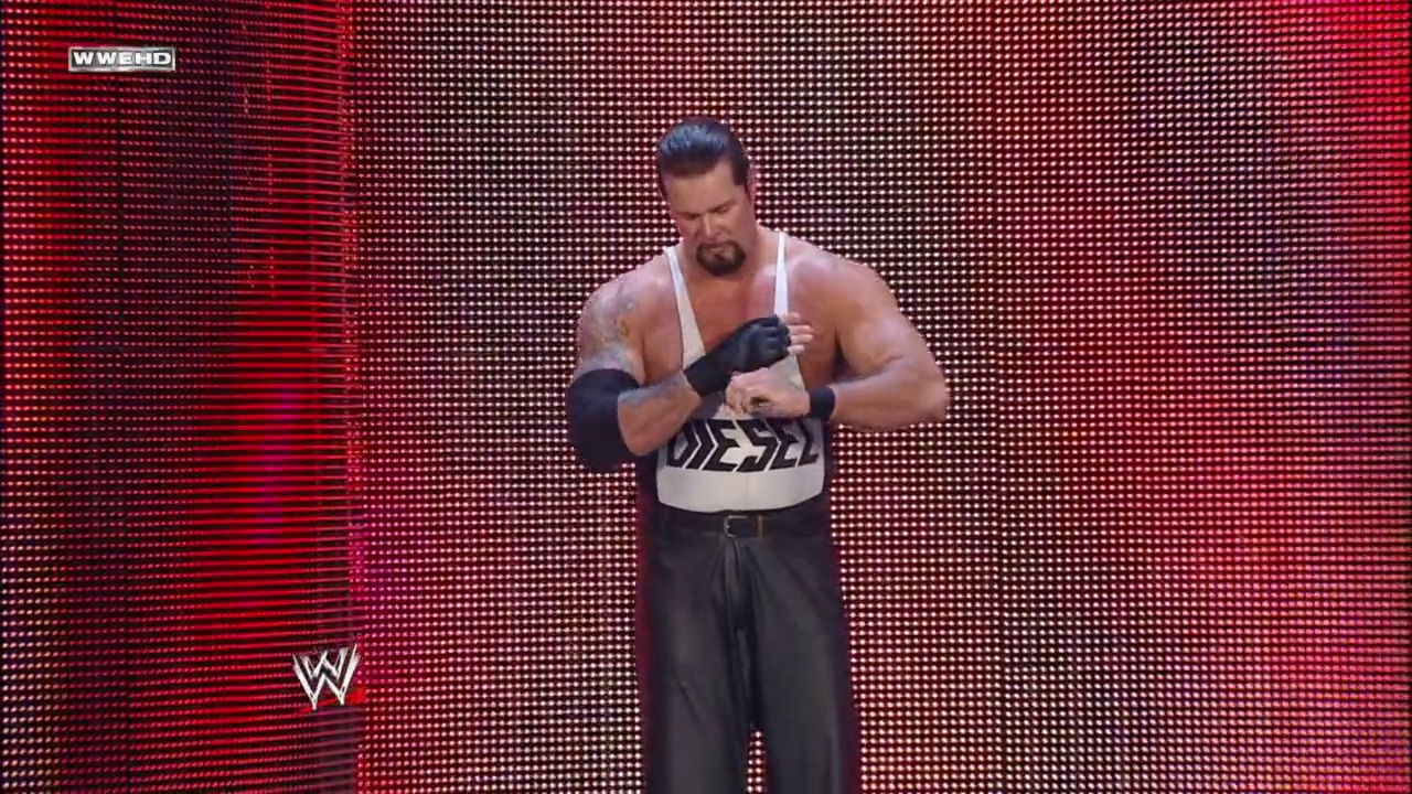 A frame from Royal Rumble (2011) at 2:19:59. A muscular wrestler in black pants and a white sleeveless top stands on a WWE ring against a bright red LED screen backdrop, adjusting his black hand wraps. The WWE logo is visible in the lower left corner.