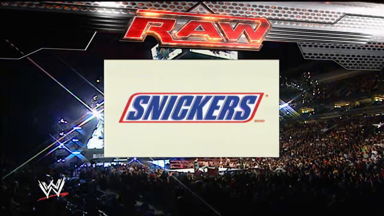 A frame from WWE Raw (October 29, 2007) at 48:42. A packed WWE arena displays the Snickers logo on the main jumbotron during Raw, with the "RAW" branding visible above and a large crowd visible in the dimly lit venue.
