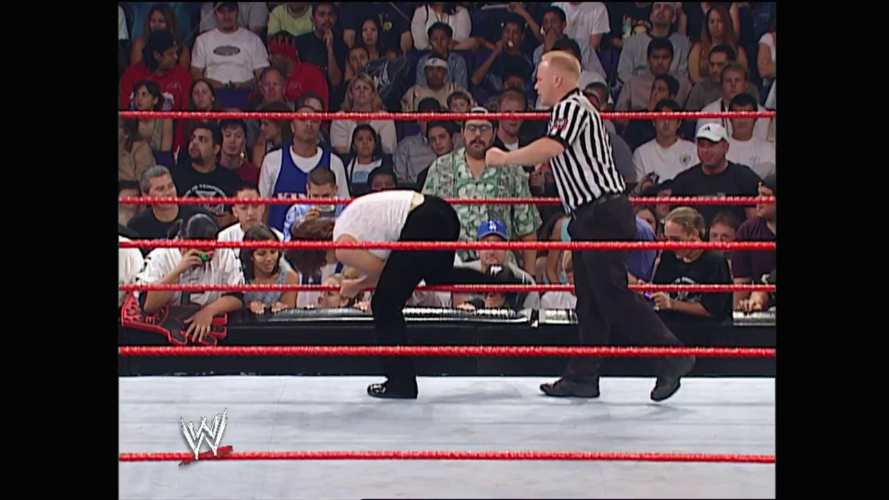 A frame from WWE Unforgiven (2002) at 1:31:10. A WWE wrestler is bent over in the ring while a referee in black and white stripes stands nearby. The red-roped wrestling ring is surrounded by a live crowd, with the WWE logo visible at the bottom of the frame.